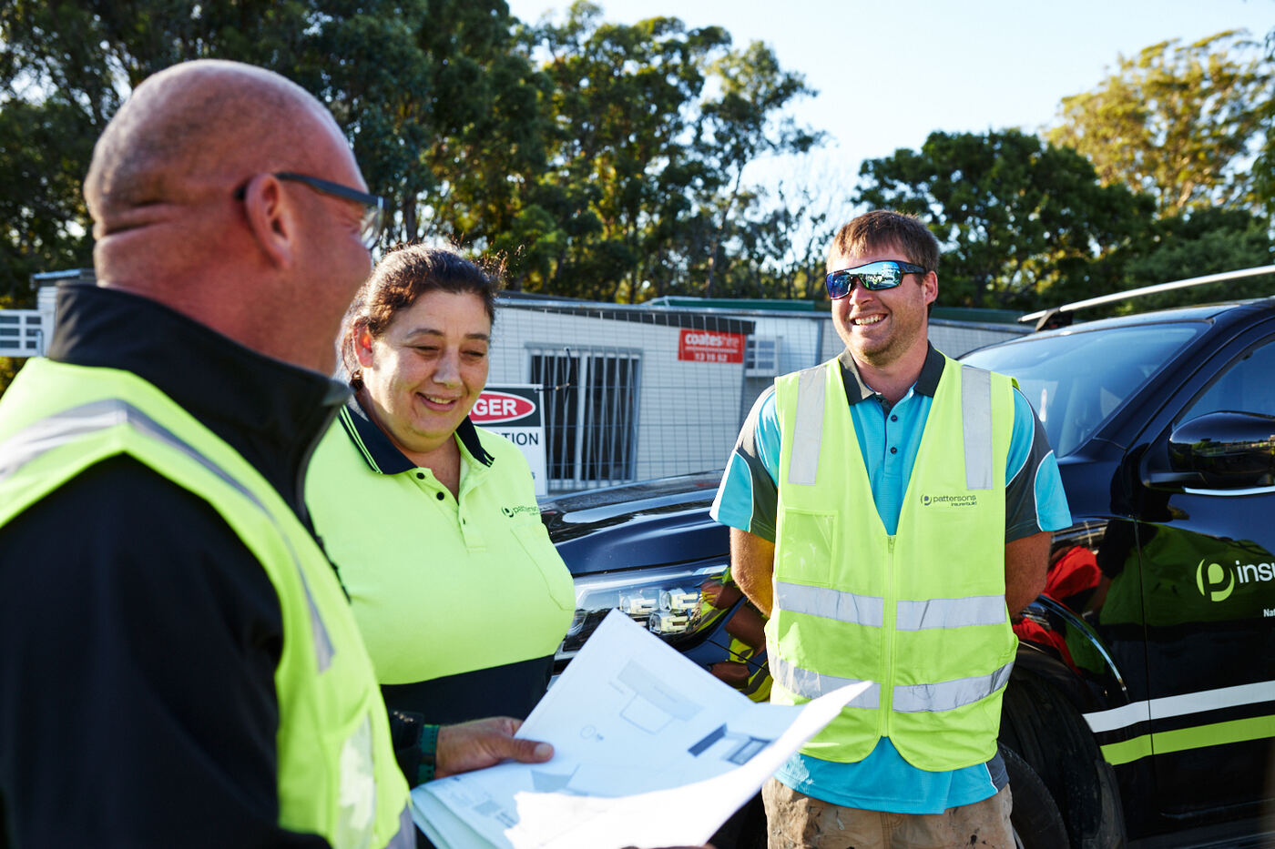 InsureBuild team in branded workwear reviewing plans beside a company vehicle on site